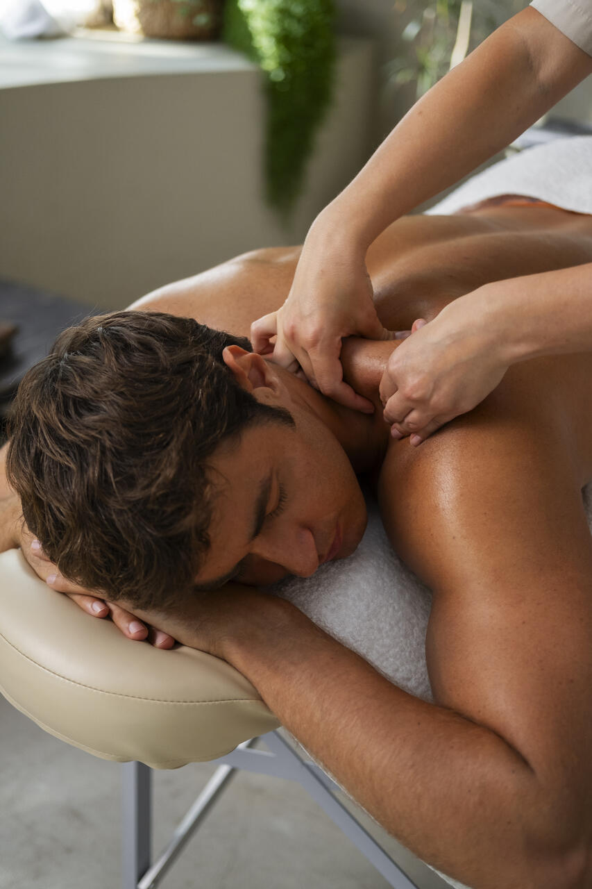 Homem deitado de bruços numa maca e mãos fazendo massagem em seu ombro