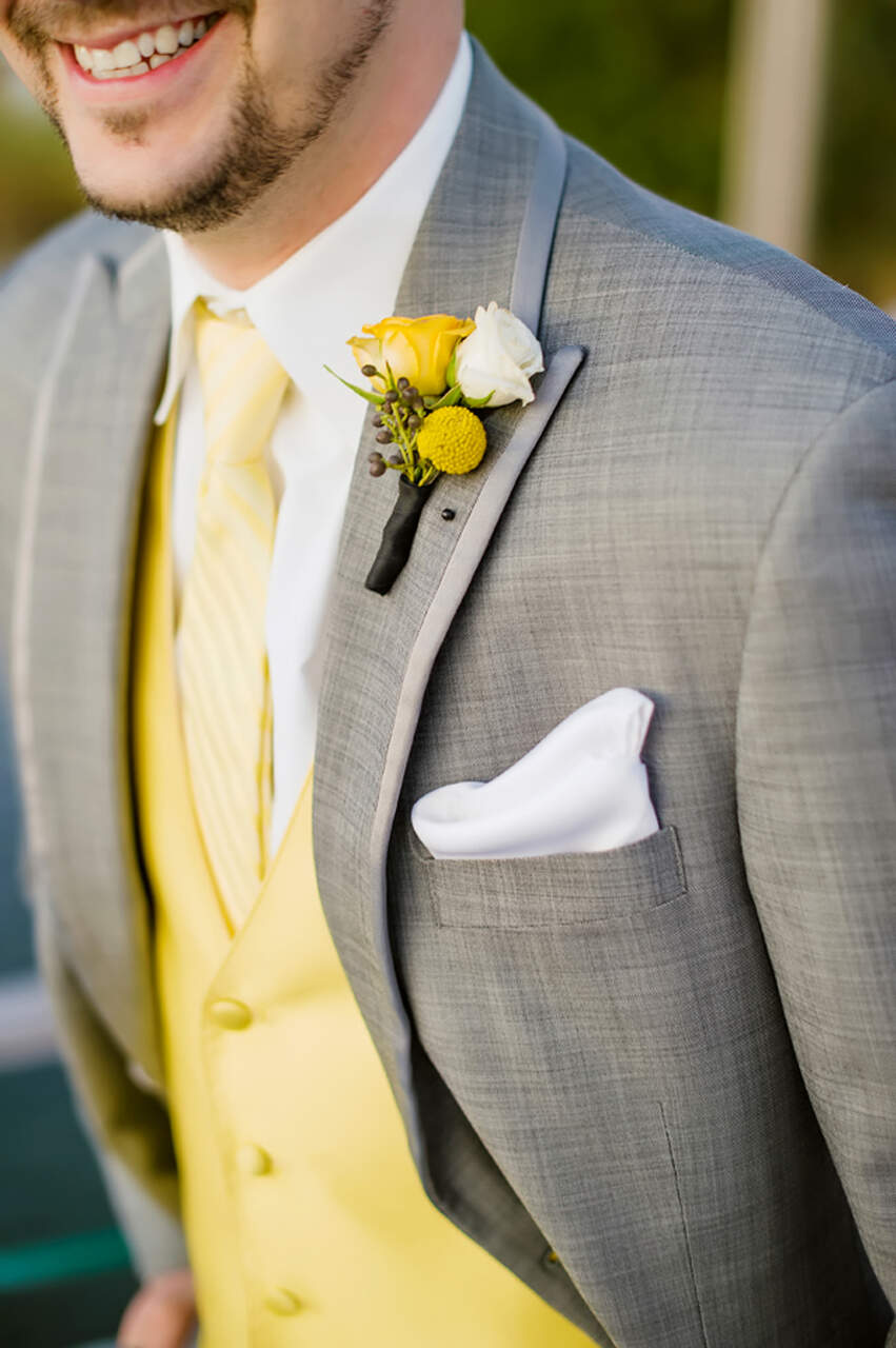 Detalhe do traje do noivo em um terno cinza claro com um colete amarelo e botonniere amarelo