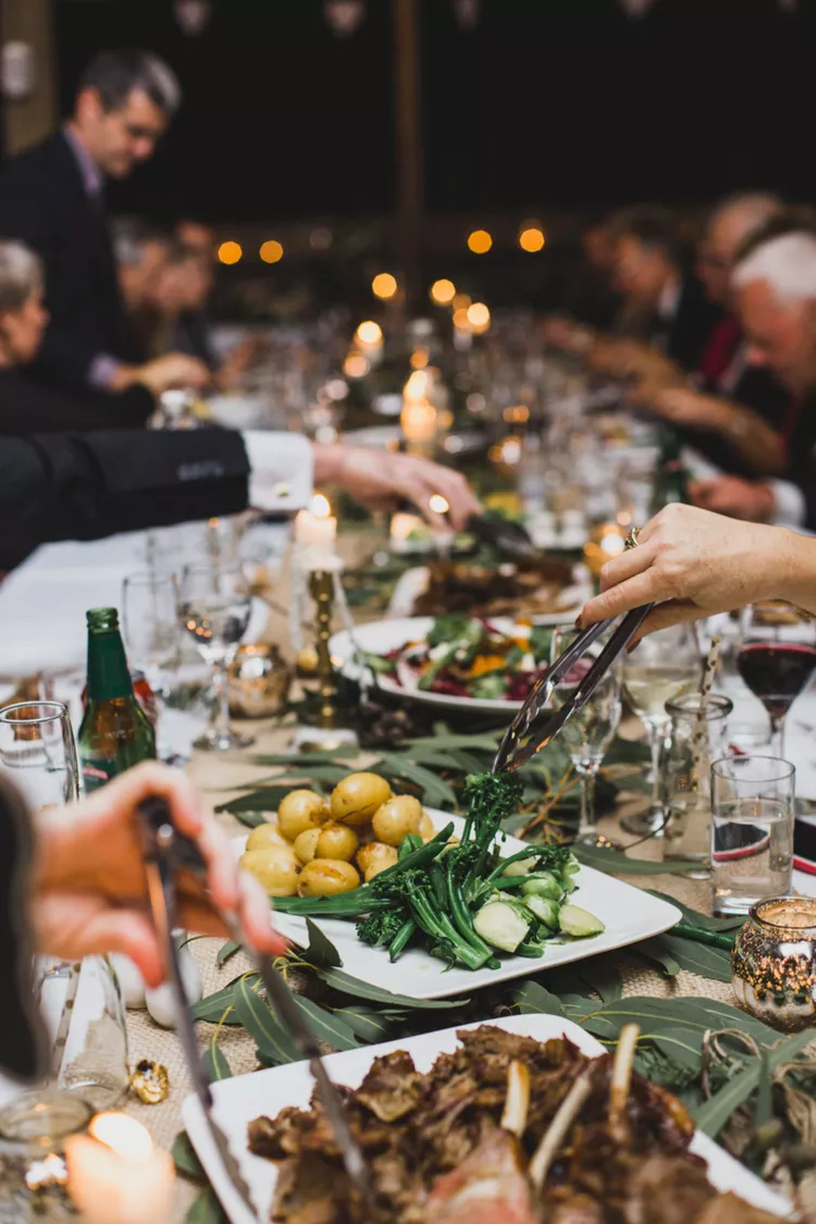 Mesa com os pratos de um jantar de casamento e alguns convidados se servindo 