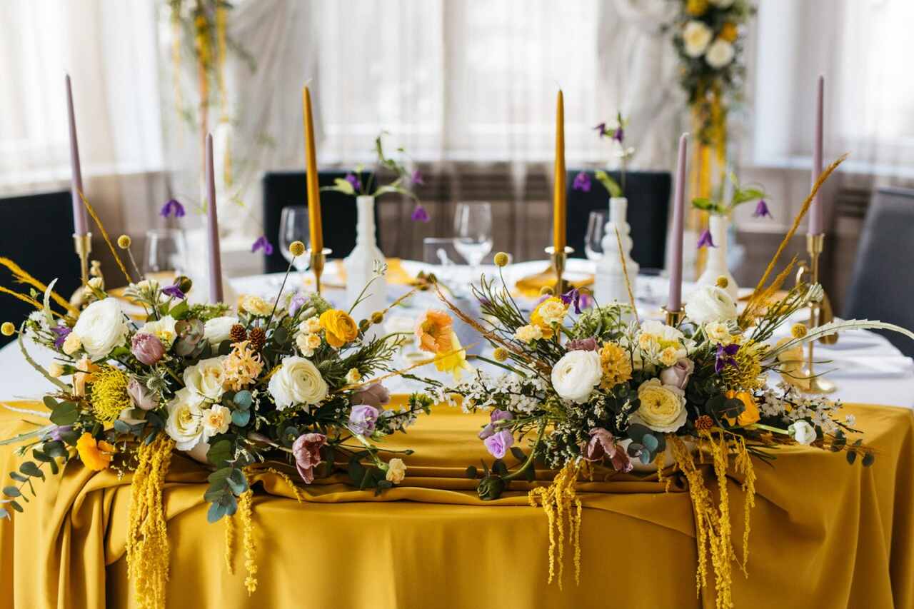 Mesa com toalha amarela, arranjos florais e velas