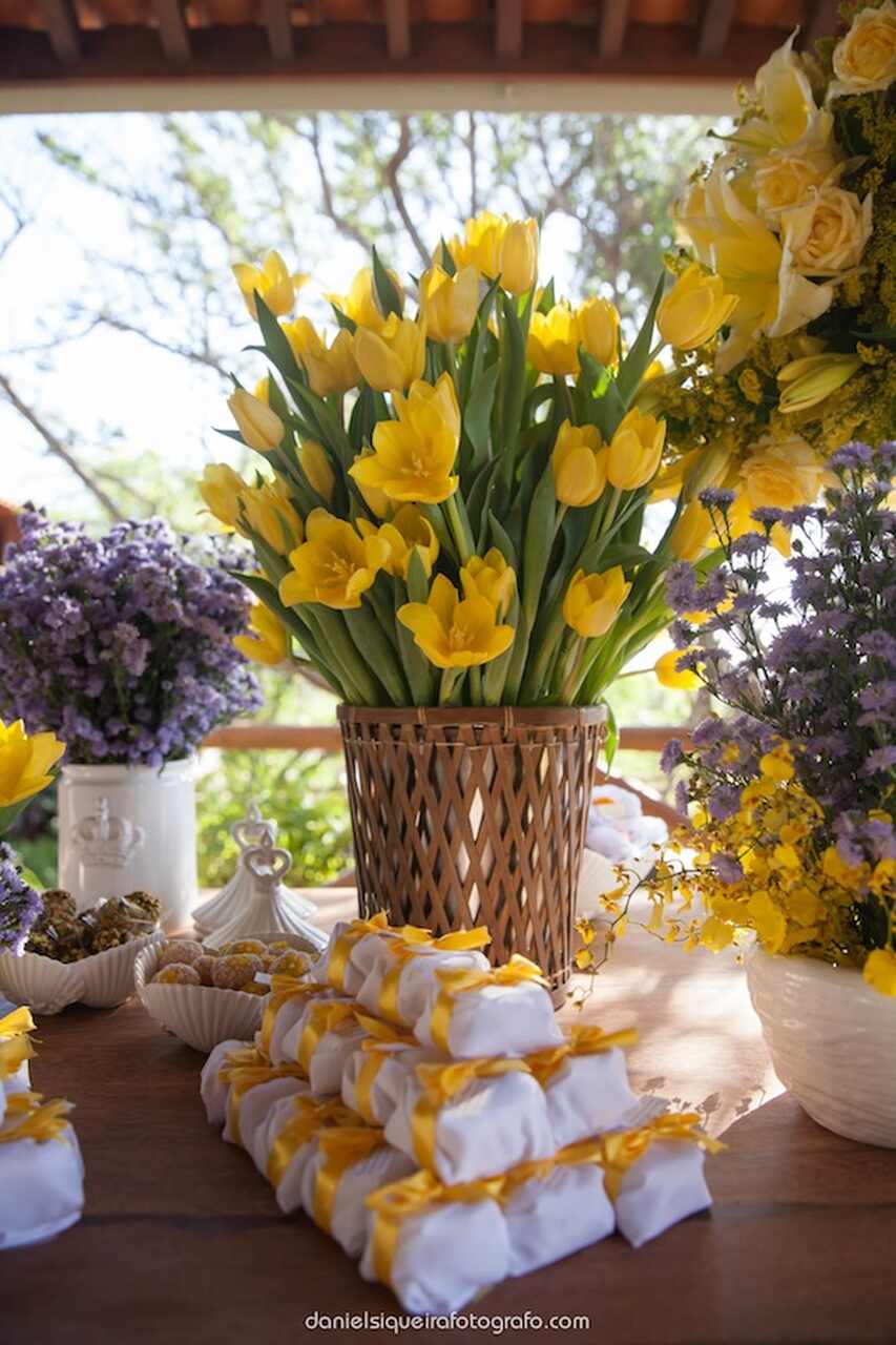 mesa com vaso de tulipas amarelas e bem casados embrulhados num papel branco com fita amarela