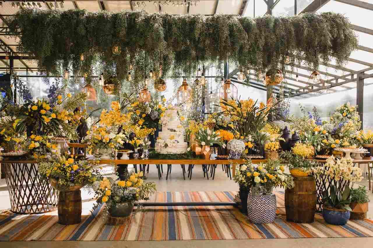 Mesa do bolo e doces com muita folhagem e flores amarelas