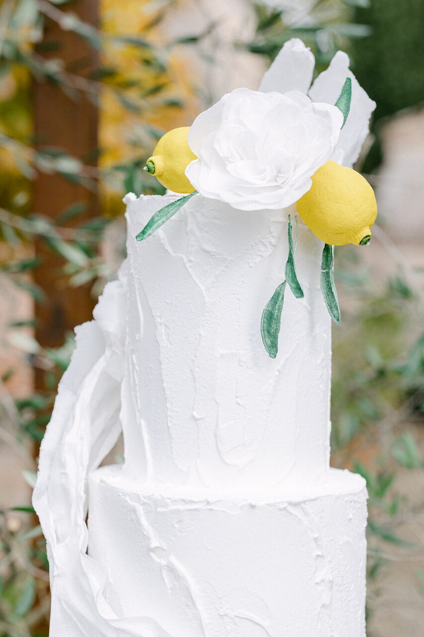 Bolo de 3 andares branco no topo com uma flor branca de limões sicilianos