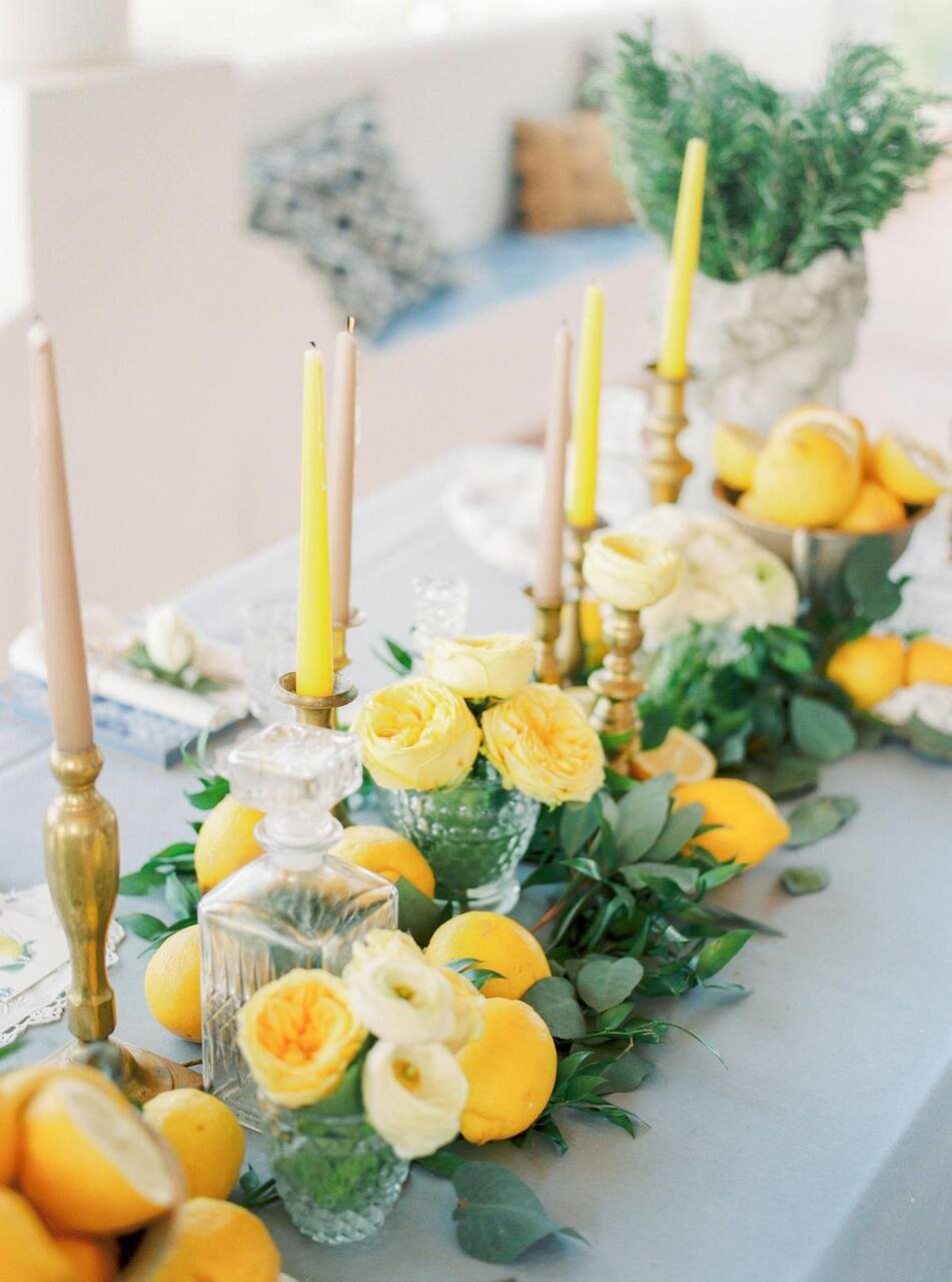 Arranjos florais amarelos sobre a mesa acompanhado de velas e limões sicilianos