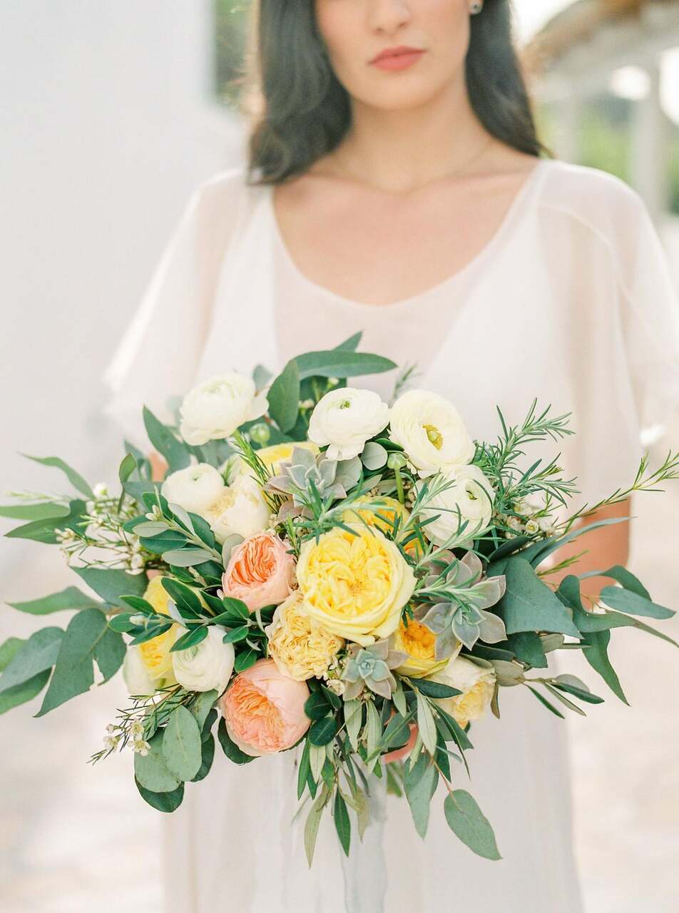 Noiva segurando buquê com flores amarelas, rosas, brancas e folhagens