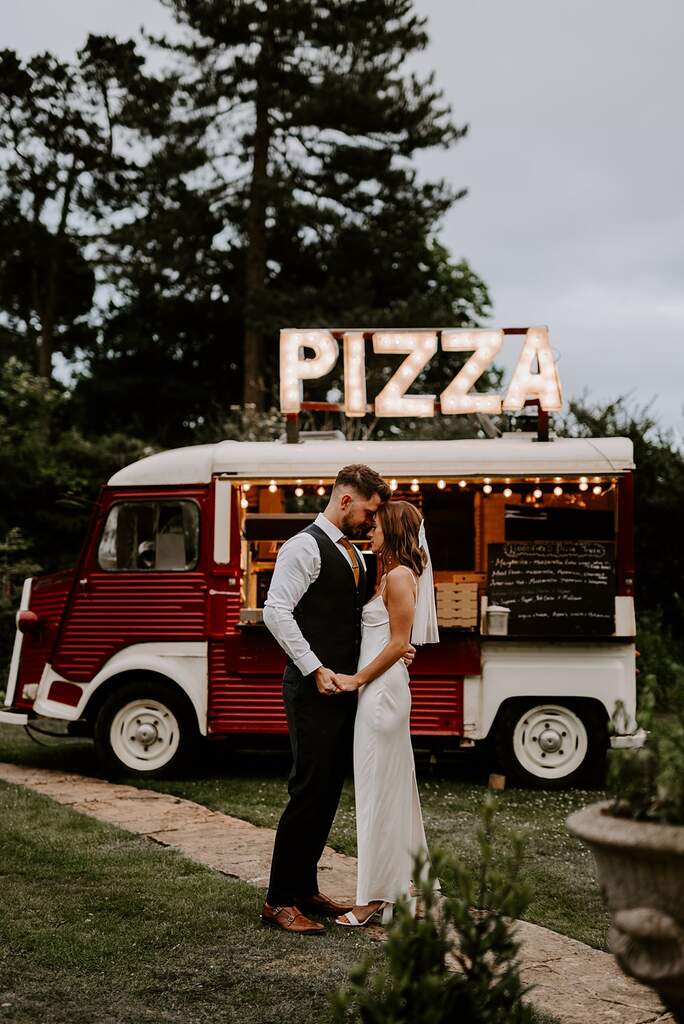 Noivos olham um para o outro com um food truck de pizza ao fundo