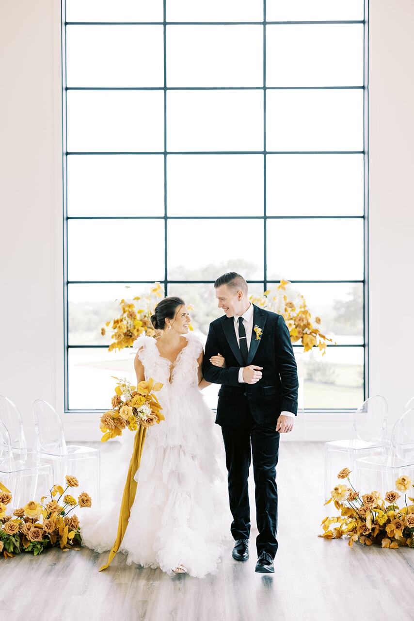 Casal no altar olhando um para o outro. Ao redor arranjos de flores amarelas combinando com o buquê da noiva