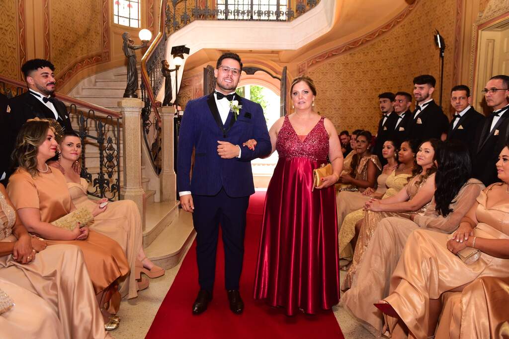 entrada do noivo com smoking azul ao lado da mãe com vestido vermelho