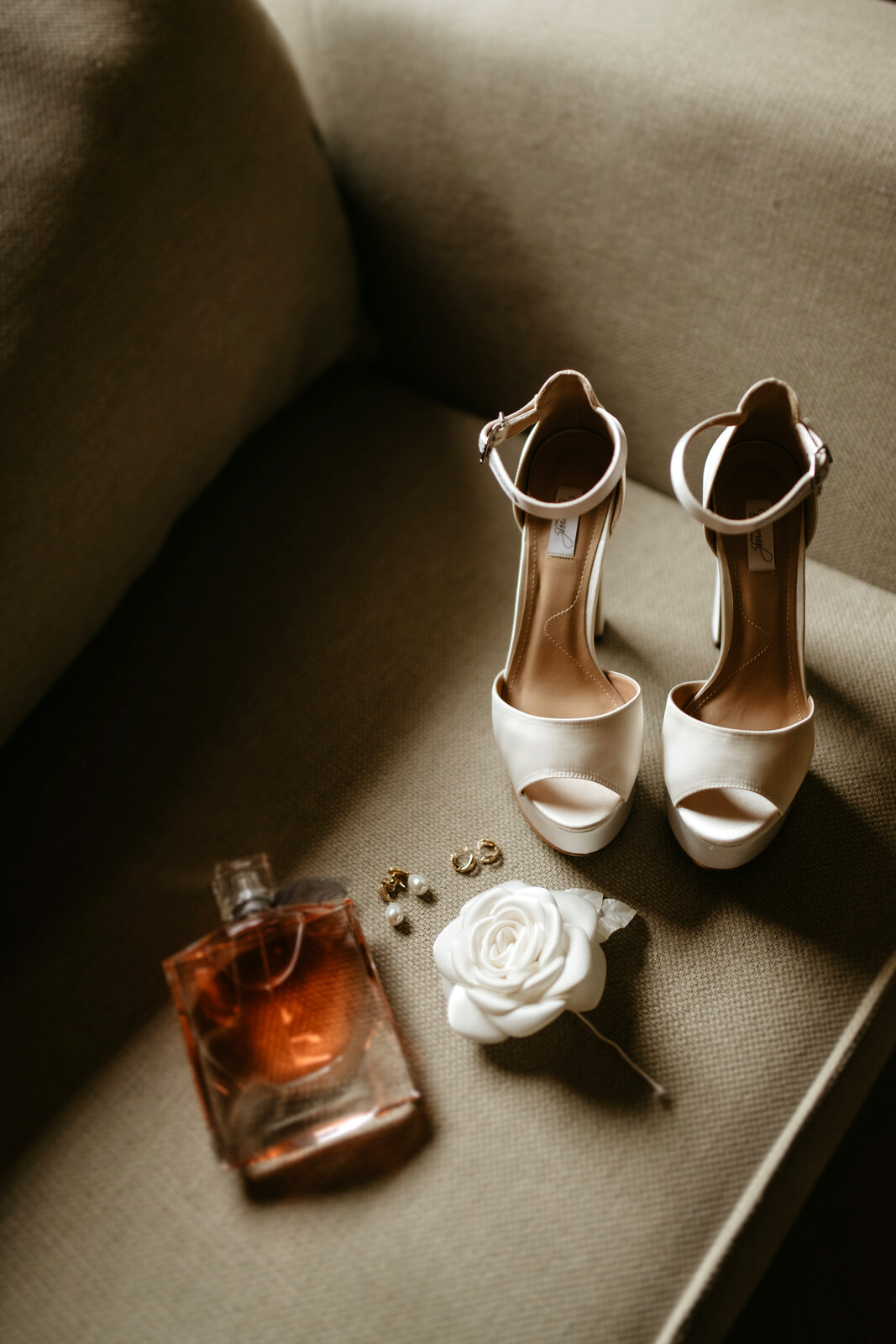sandália peep toe branca da noiva ao lado de brincos perfume e flor branca