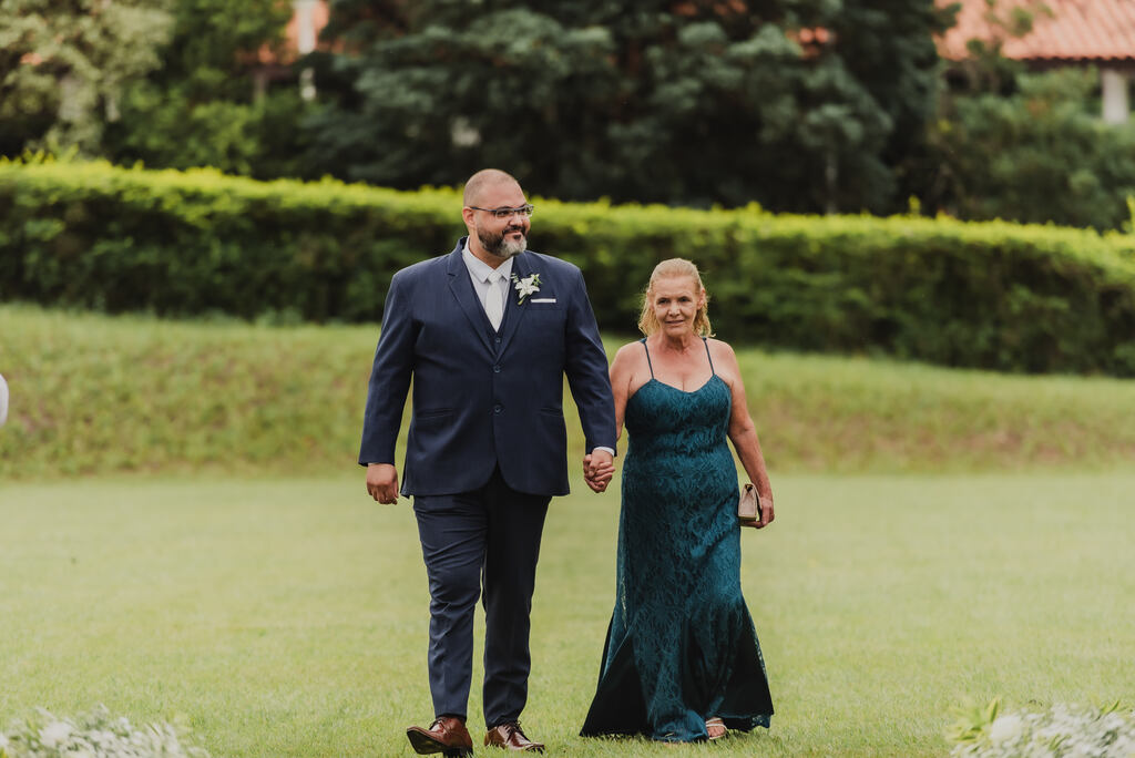 entrada do noivo com terno azul de mãos dadas com a mãe com vestido verde de alcinha