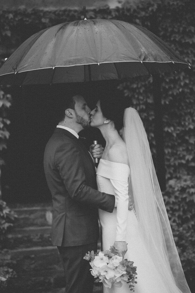 Noivos se beijando embaixo de um guarda-chuva