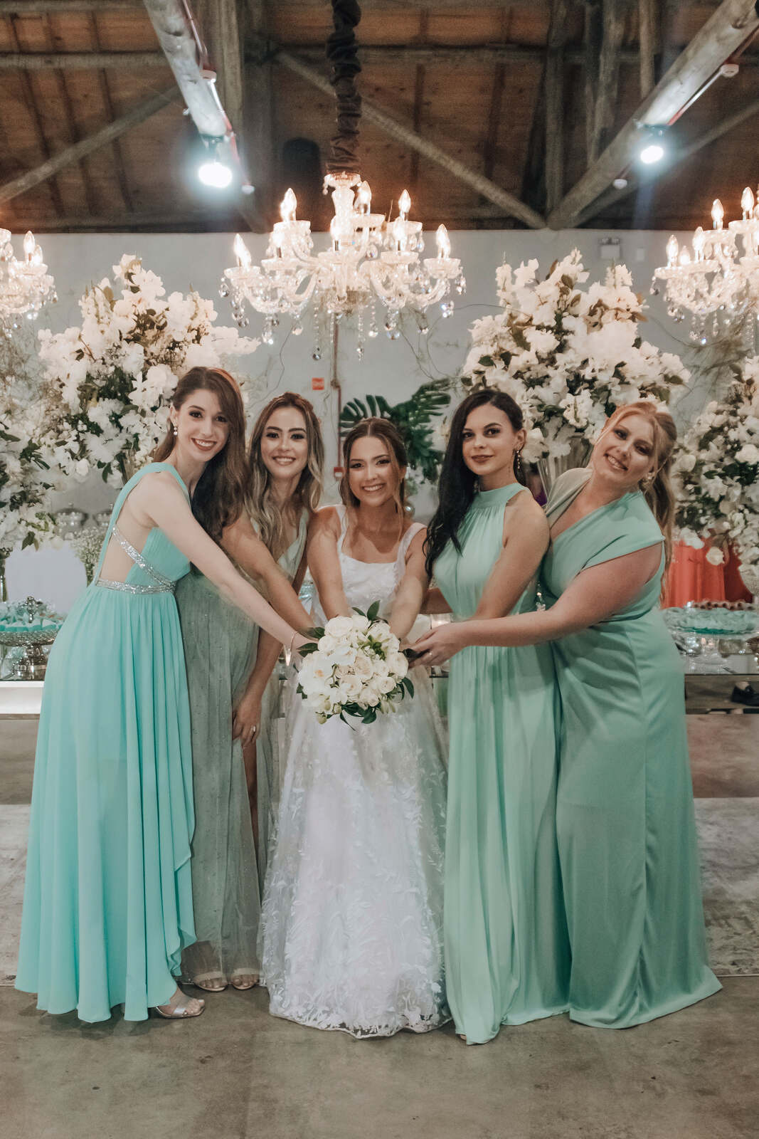 Noiva e suas madrinhas com vestidos verde claro posam para uma foto em frente a um candelabro