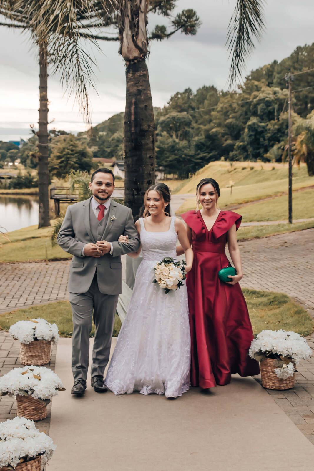 entrada da noiva ao lado do pai com terno cinza e garavat vermelha e mãe com vestido vermelho