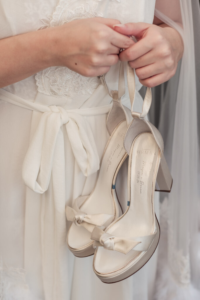 noiva com robe branco segurando sandália de salto