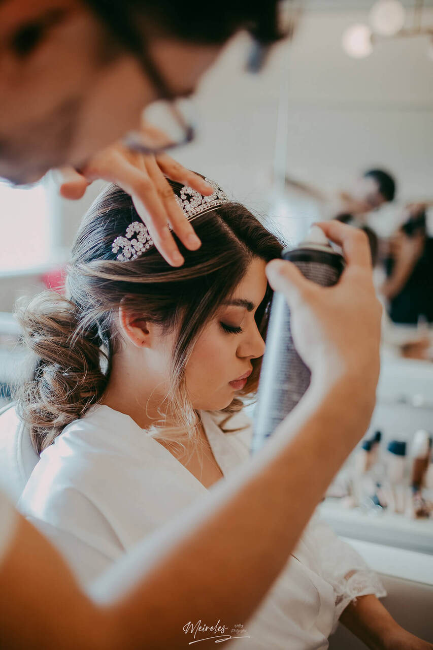 Profissional finalizando o penteado da noiva com um spray