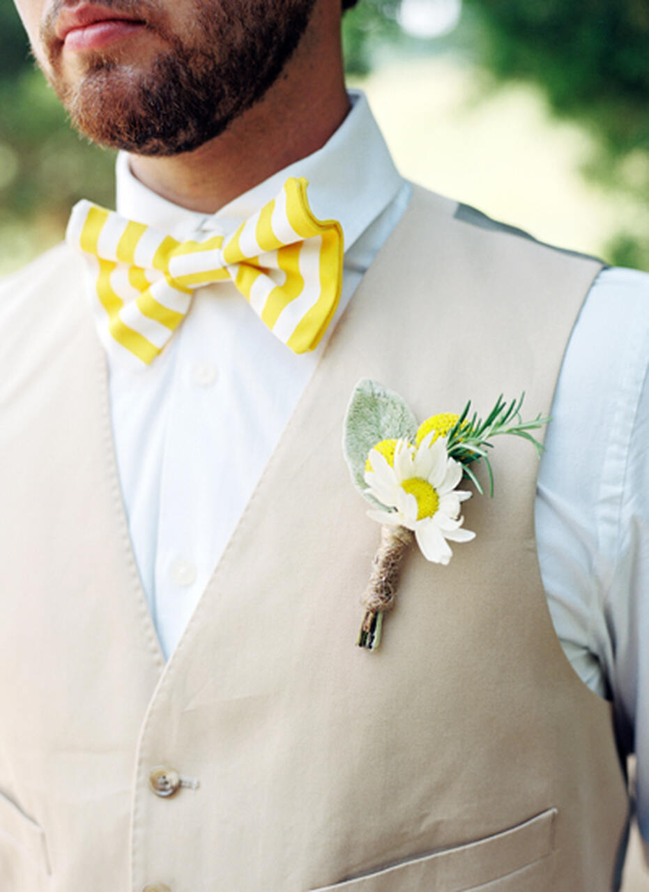 Detalhes do traje do noivo, com gravata borboleta listrada amarela e branca e boutonniere com uma flor branca