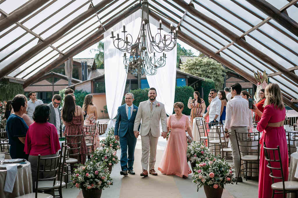 entrada do noivo com a mãe com vestido rosa claore pai com terno azul