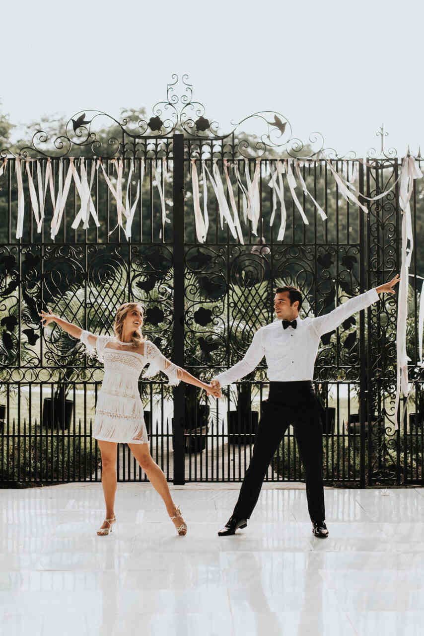 Noivos se olham e fazem pose com uma das mãos levantadas para apresentação de dança no casamento 