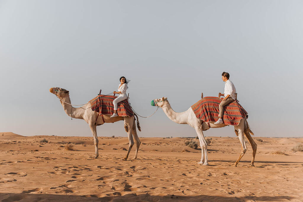 casal em lua de mel em dubai andando de camelo no deserto