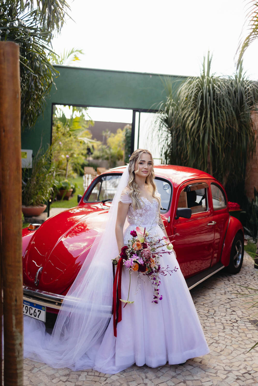 noiva com buquê rosa na frente de fusca vermelho