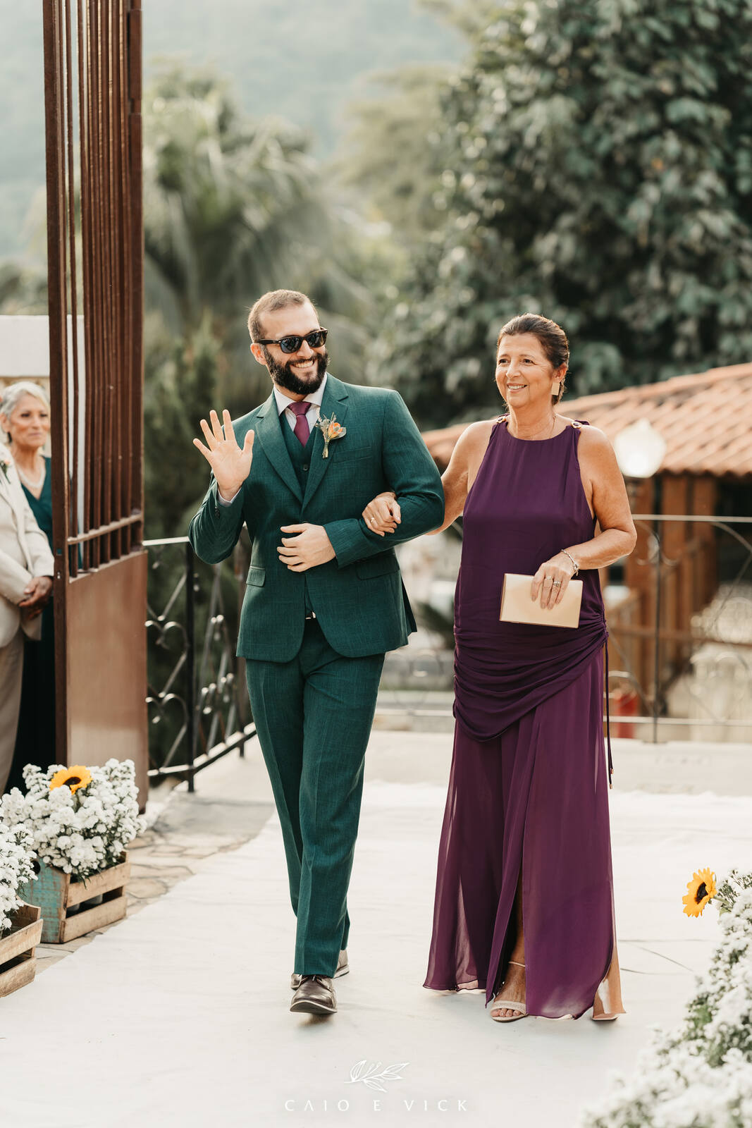 entrada do noivo com terno verde e mãe com vestido roxo