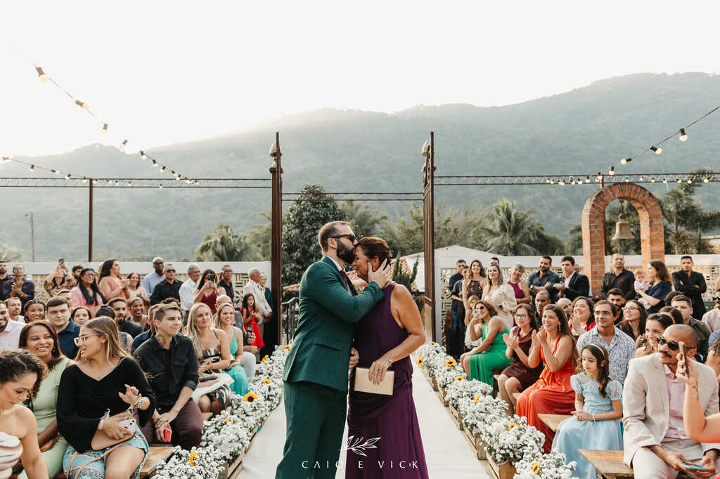 entrada do noivo com terno verde e mãe com vestido roxo