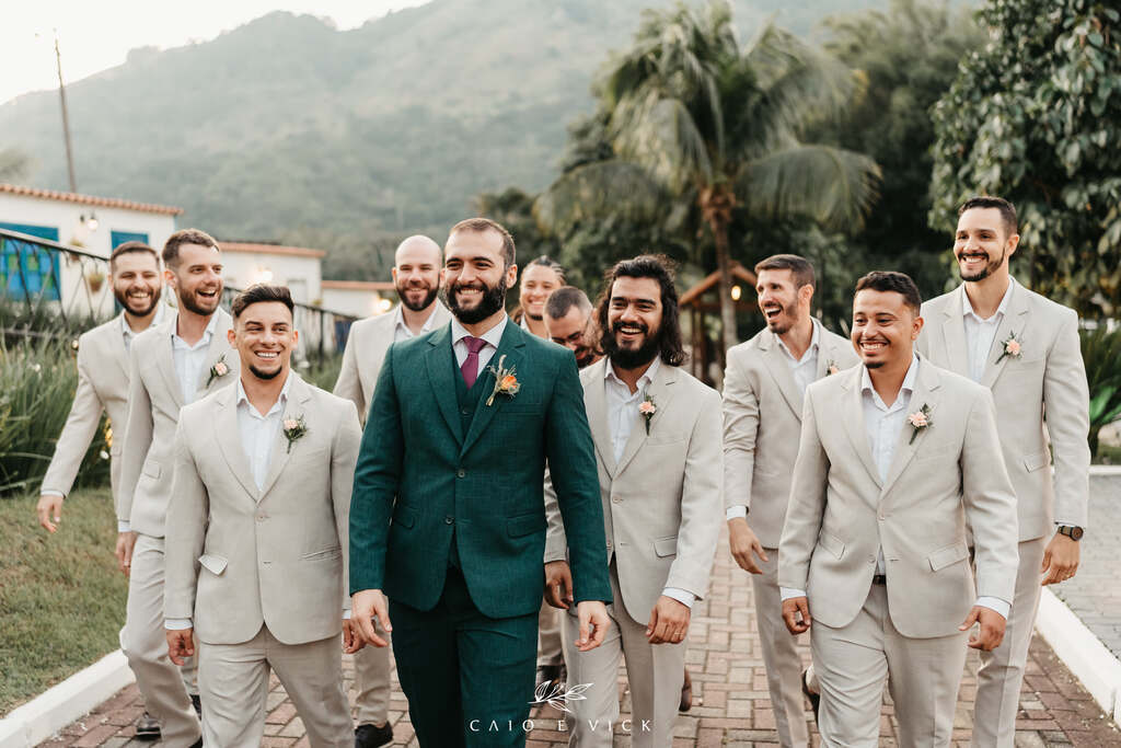 noivo com tenro verde ao lado dos padrinhos com terno cinza