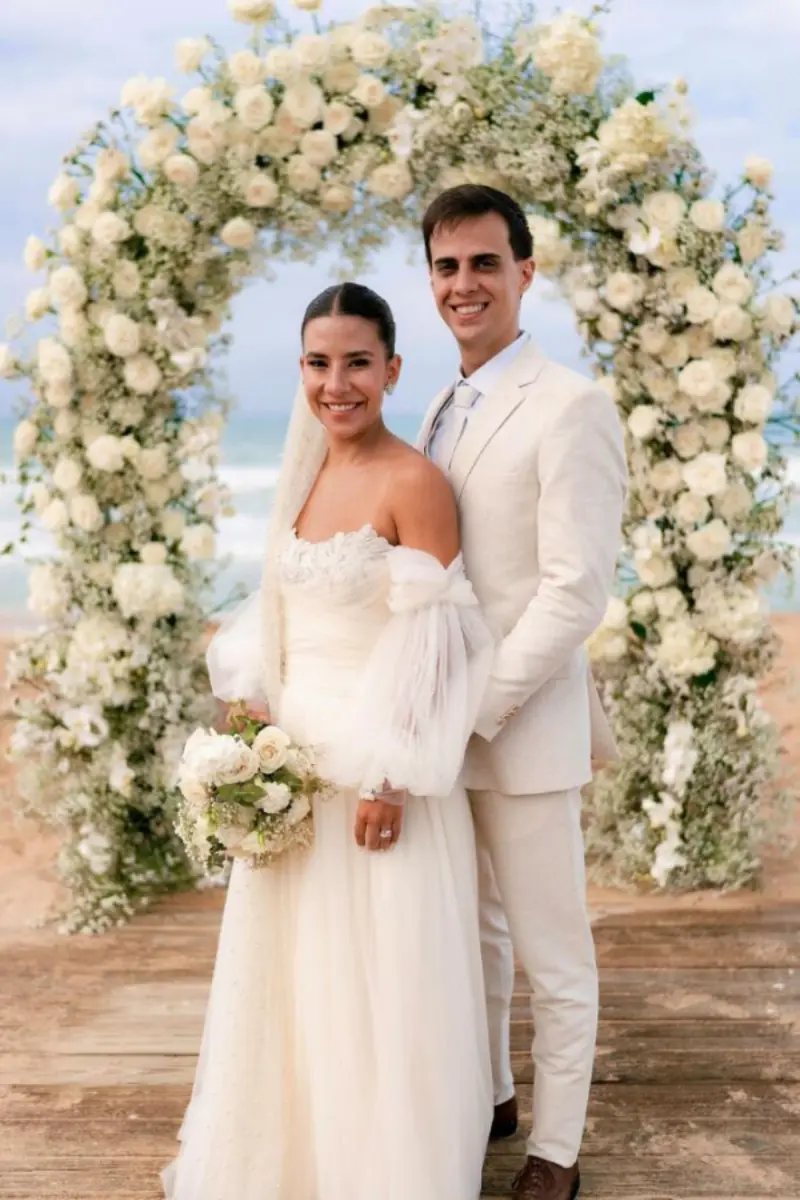 noivos posando em pergolado com arranjo florais brancos