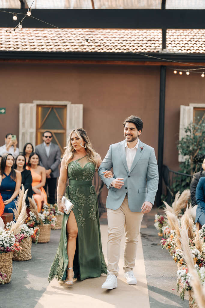 entrada do noivo com terno azul e calça bege ao lado da mãe com vestido verde