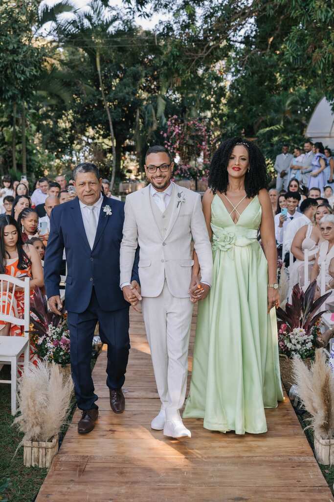 entrada do noivo com o pai com terno azul e mãe com vestido verde claro