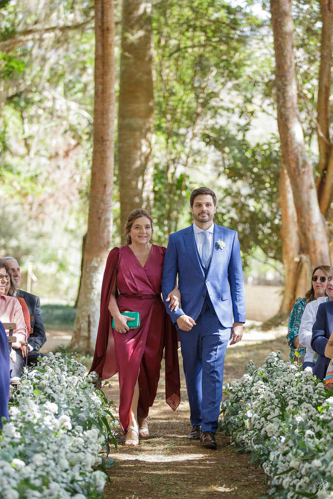 Noivo entrando na cerimônia com a mãe de vestido bordô e bolsa de mão verde