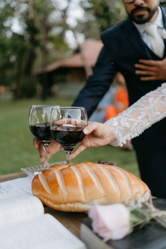 Noivos pegam taças de vinho da Santa Ceia. Sobre a mesa está um pão