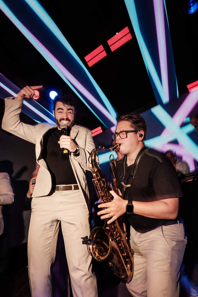 Cantor e saxofonista animando o público na pista de dança, com iluminação colorida