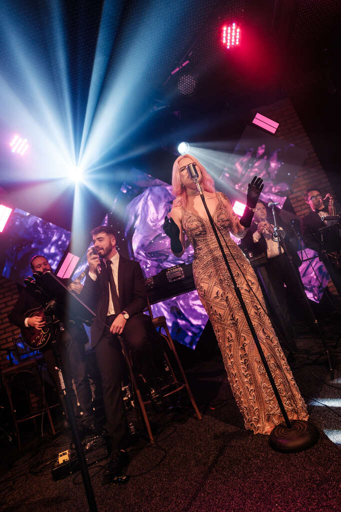 Cantora e banda ao vivo se apresentando em um palco de casamento, com iluminação de fundo vibrante