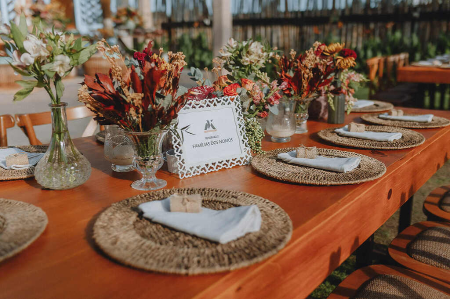 Mesa dos convidados com sousplats, arranjos florais e um quadrinho escrito Família dos noivos