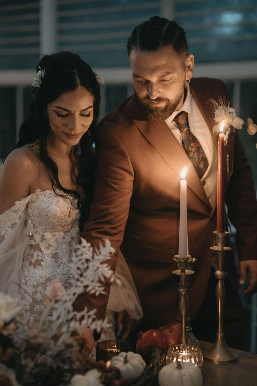 Casal de noivos acendendo velas em uma mesa decorada com flores e frutas