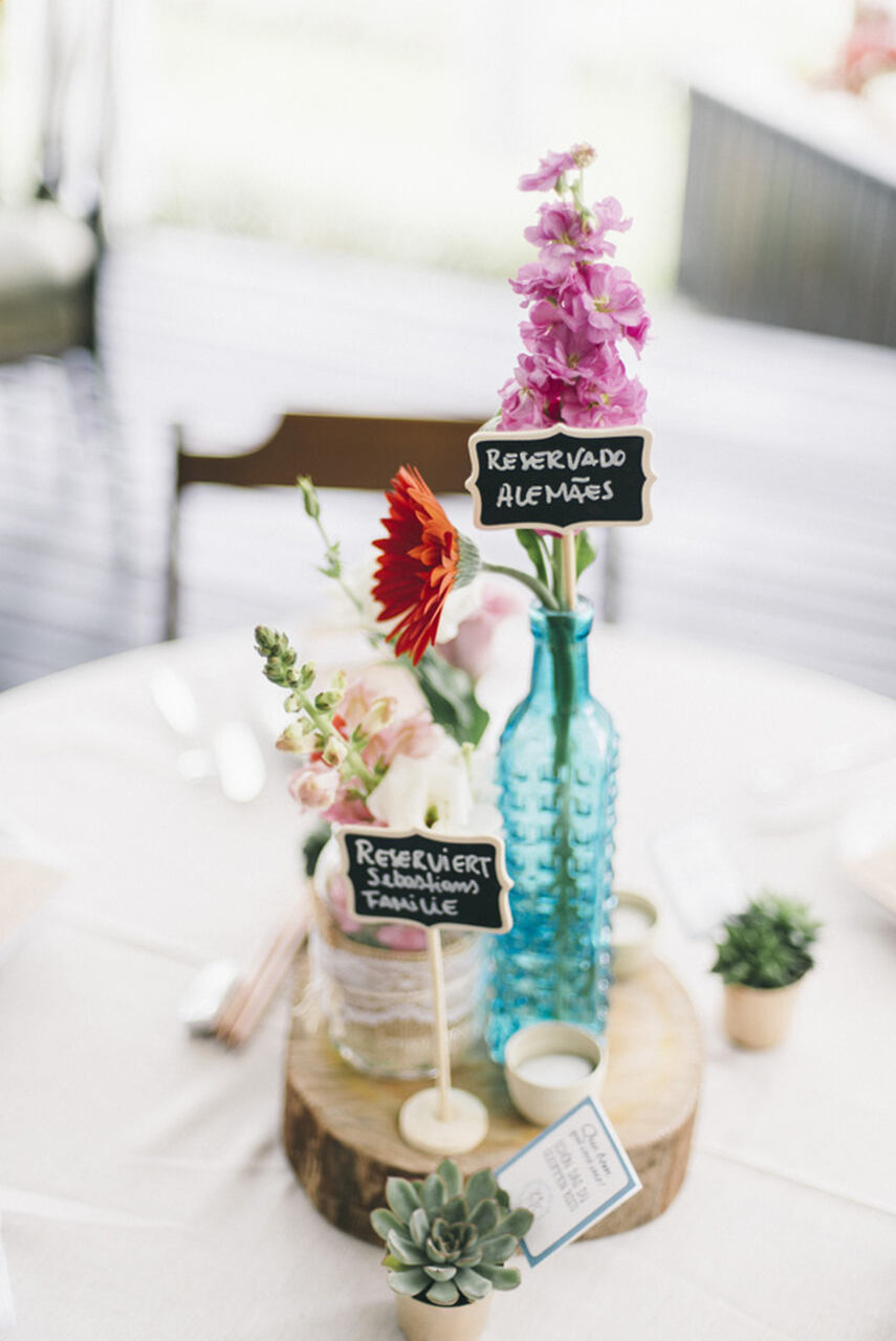 Decoração de mesa ao centro com garrafas com flores dentro e plaquinhas