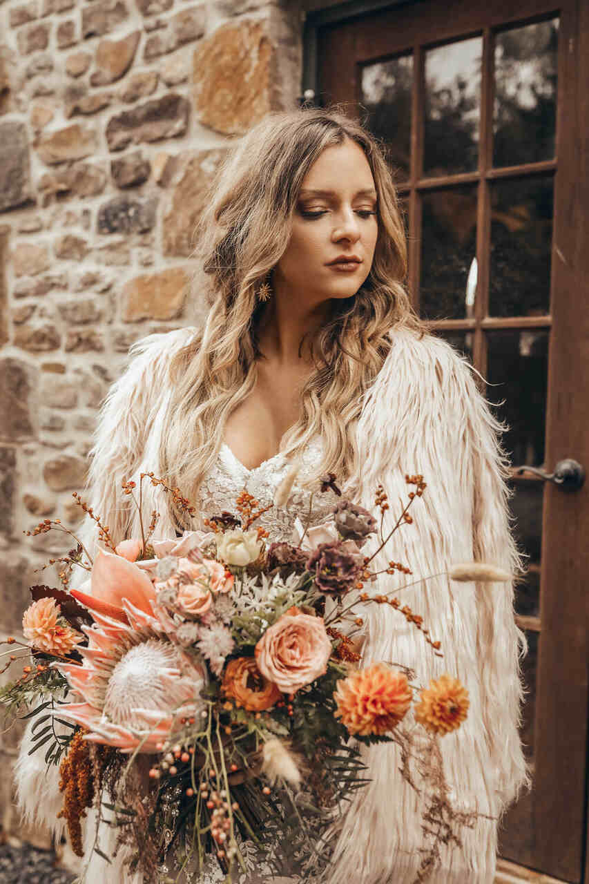 Noiva segurando um buquê de flores, de vestido com uma capa de pêlos