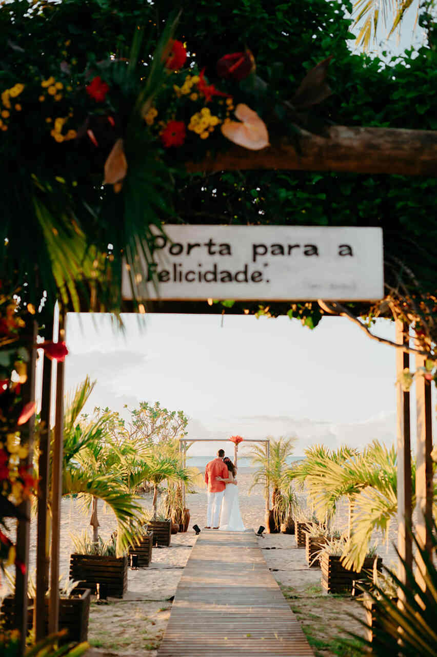 Placa pendurada na entrada na cerimônia escrita: Porta para a felicidade. Ao fundo, no altar, os noivos abraçados