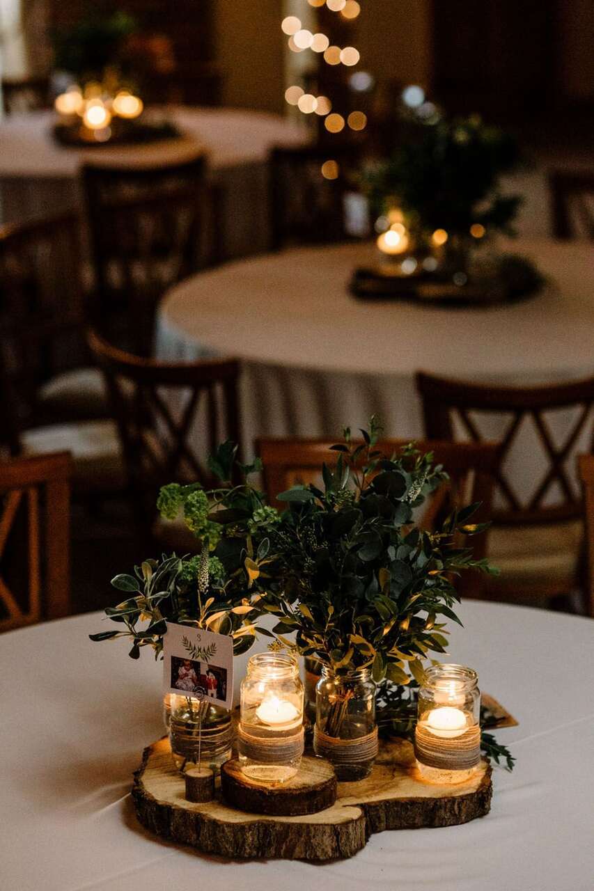 Arranjo de mesa com a base de tronco de madeira. Em cima, velas e vasos de folhas