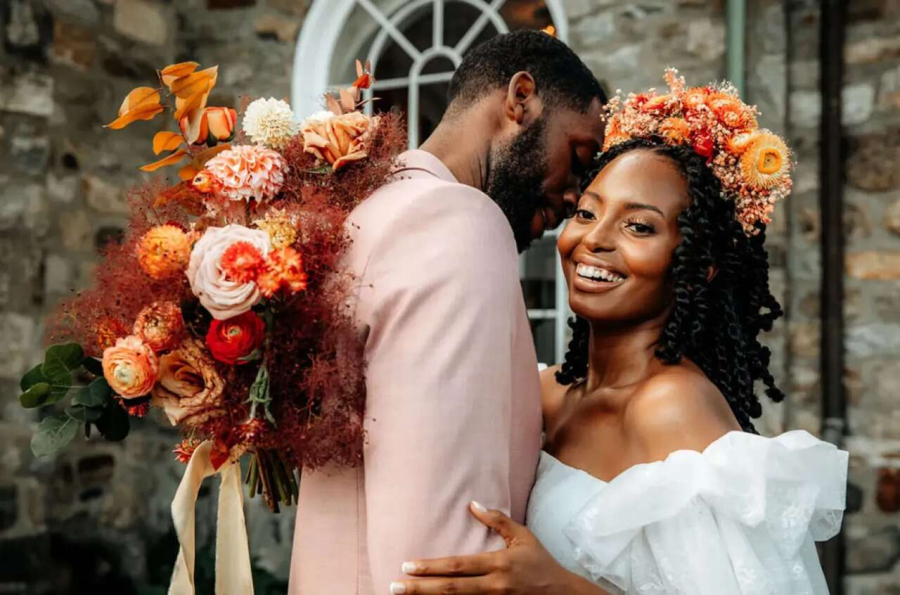 Noivos se abraçando. Noiva mais em evidência com coroa de flores na cabeça e buquê em uma das mãos