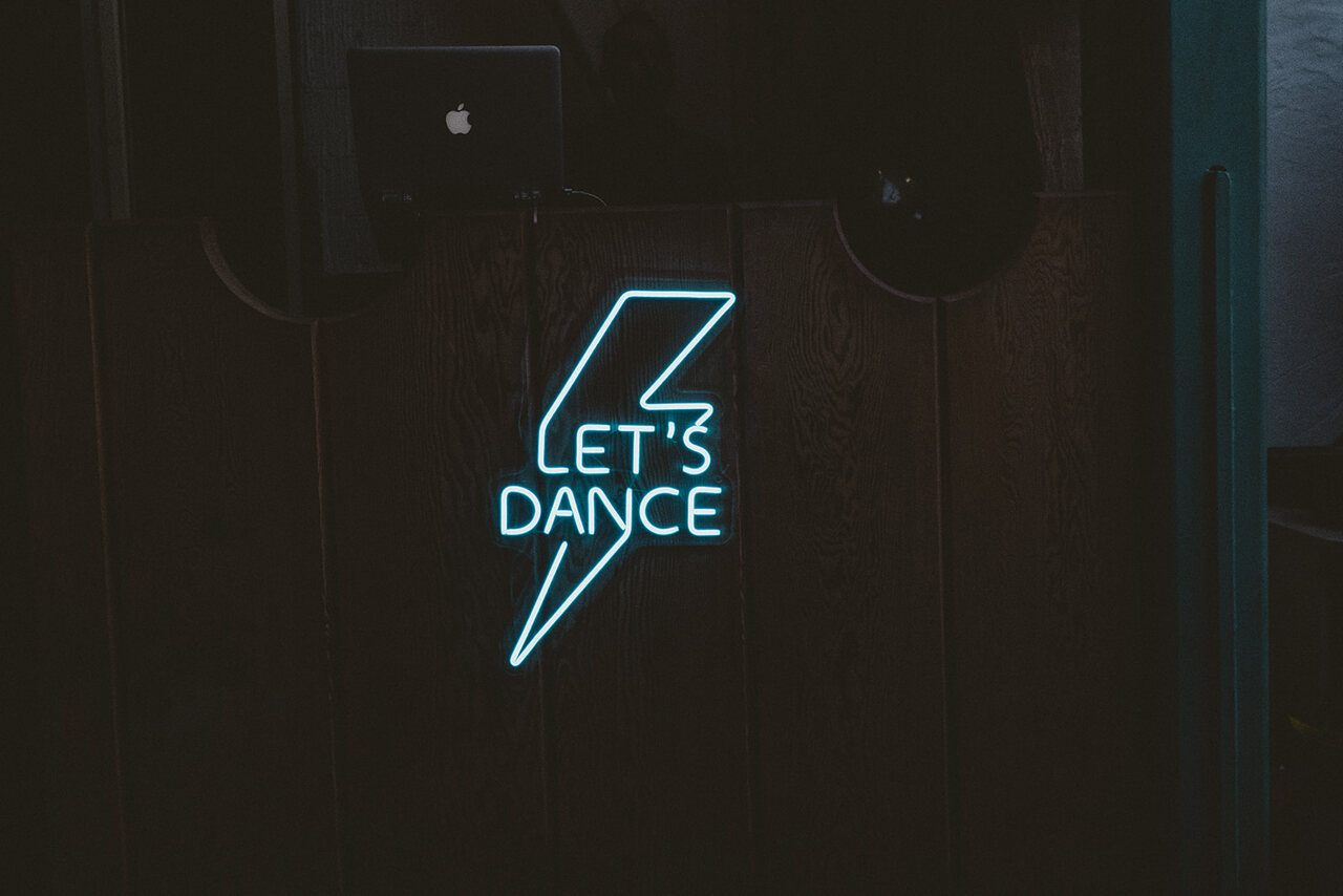 Letreiro de neon azul com a frase 'Let's Dance', iluminando a área da pista de dança em uma festa de casamento.