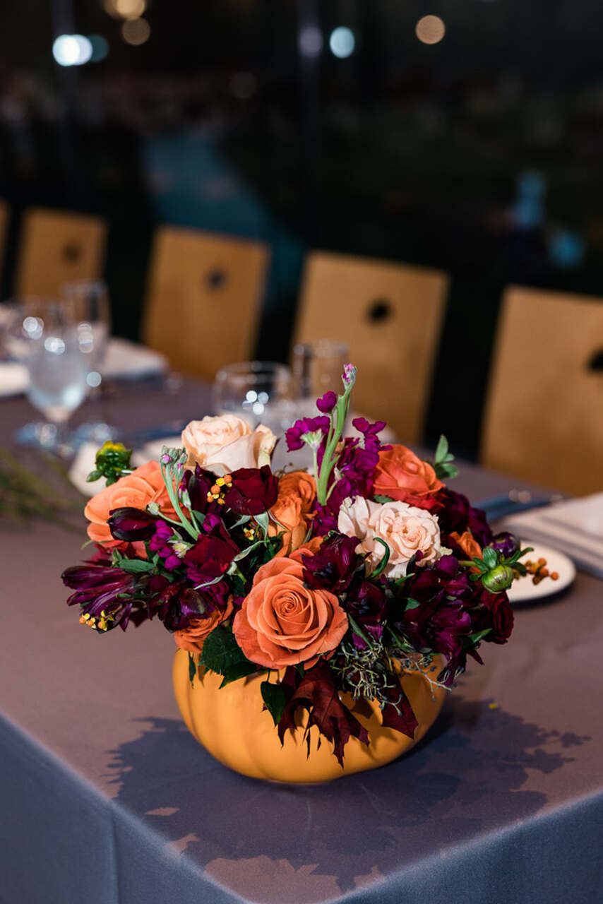 Arranjo de mesa com flores e folhas dentro de uma abóbora usada como vaso