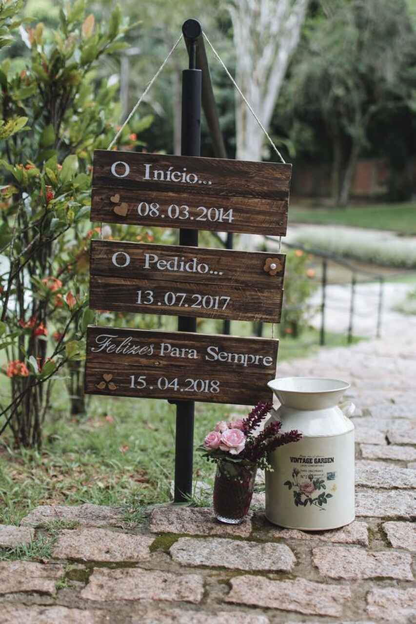 Placa fincada no chão, com 3 partes. Uma escrita a data do início do relacionamento, outra com a data do pedido e a última com a data do casamento