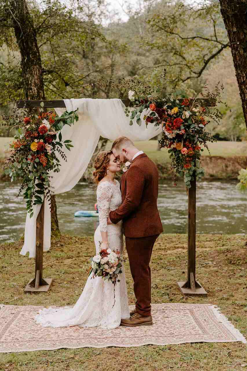 Casal no altar de frente um para o outro e com o rosto próximo. Ao fundo um altar em madeira com arranjos de flores