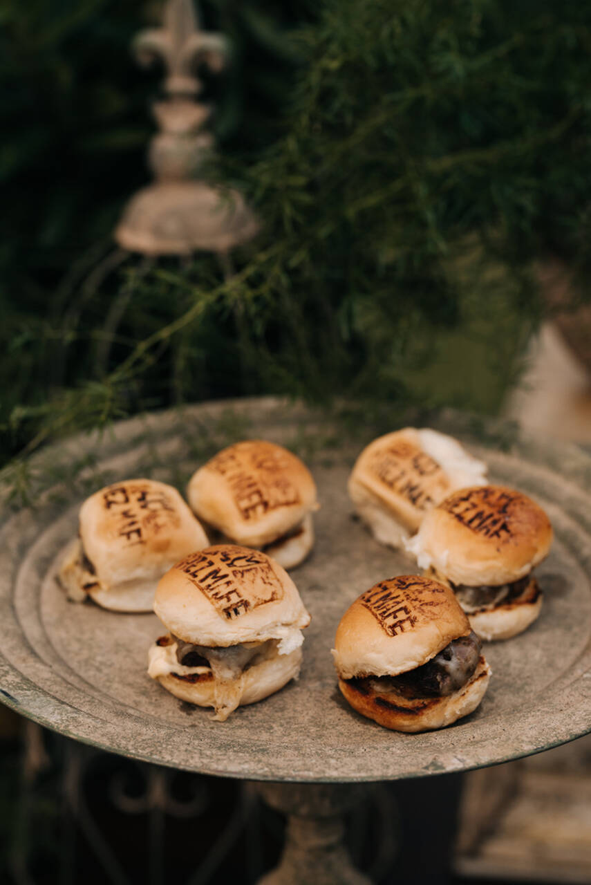 Mini hambúrgueres servidos em uma bandeja rústica, com os pães personalizados com nomes gravados na superfície