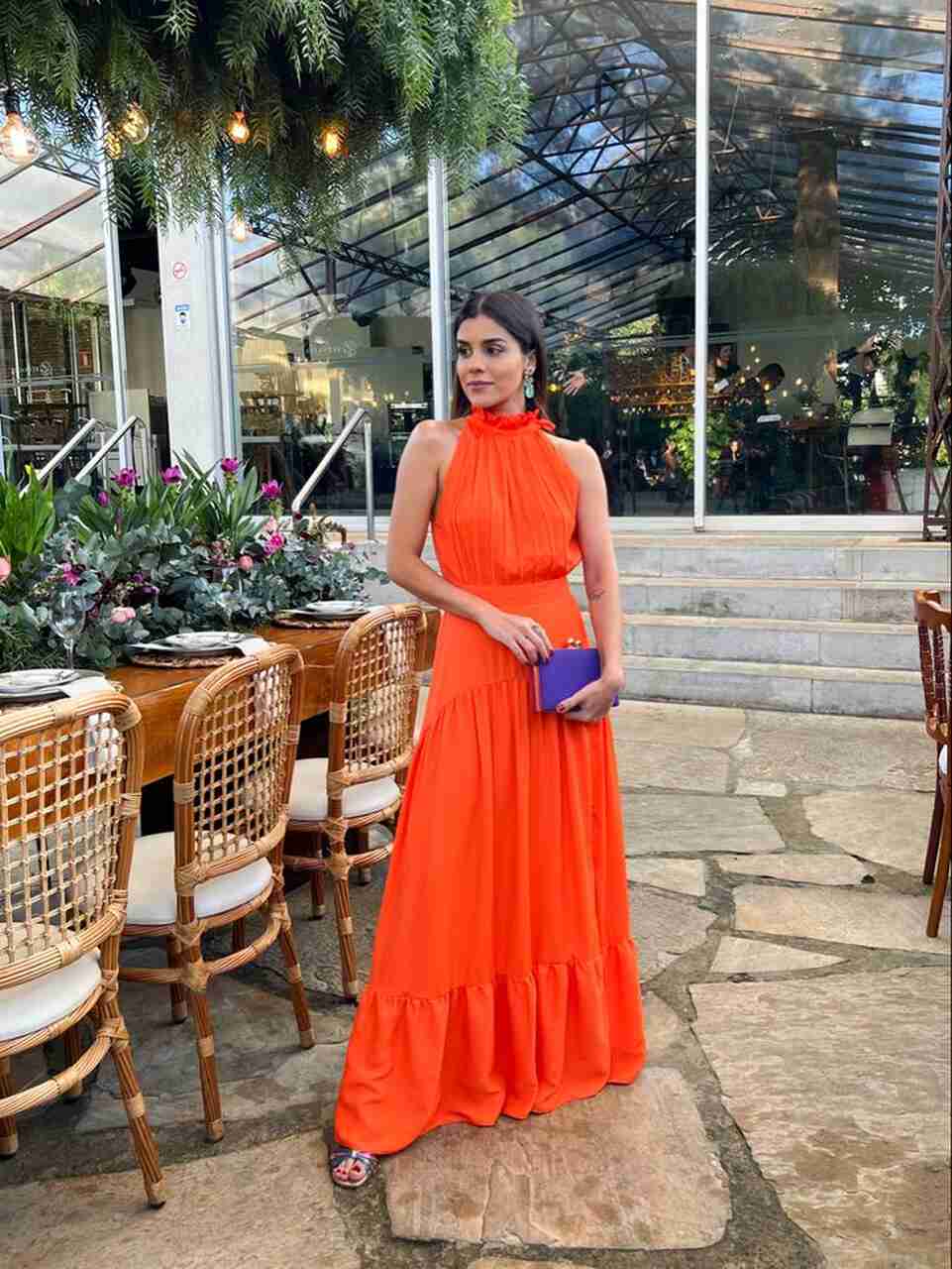 Mulher com vestido laranja vibrante e uma bolsa de mão roxa