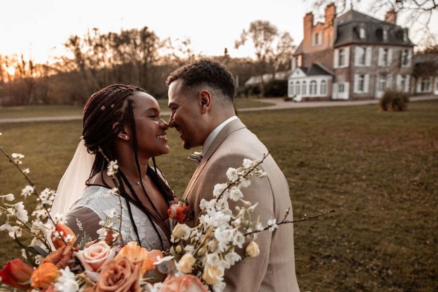 Casal sorrindo olhando um para o outro, com os rostos aproximados, em um cenário a céu aberto com uma casa ao fundo