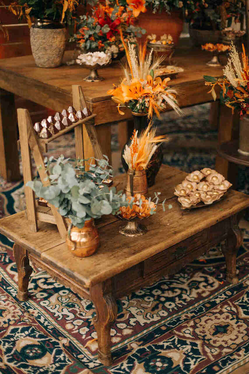 Mesa de decoração em madeira, com vaso, folhas, flores e doces