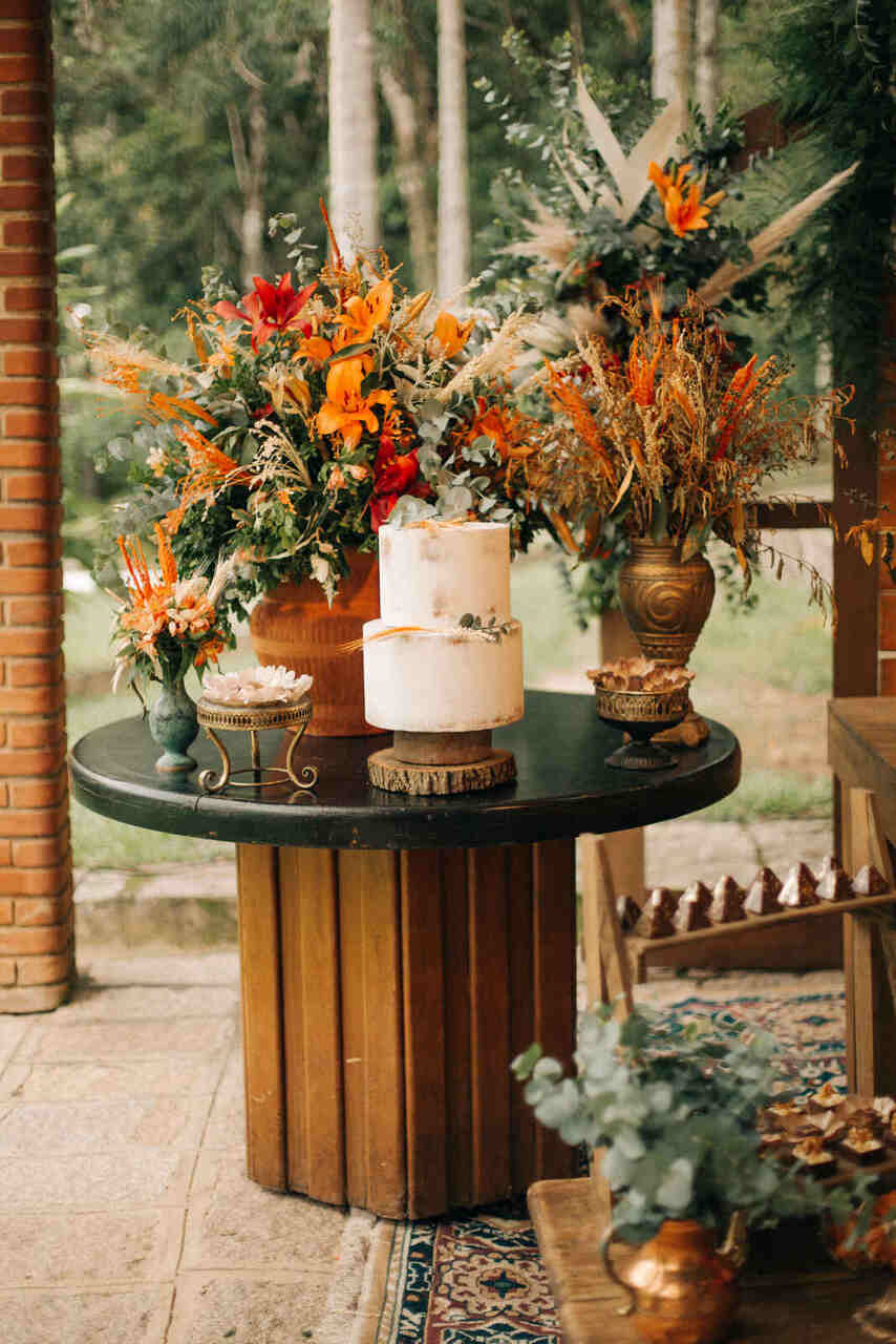 Mesa do bolo com detalhes em madeira e arranjos com flores e folhagens